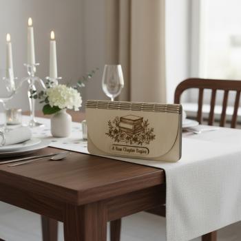 Holz-Umschlag aus hellem Birkensperrholz mit gelaserter Gravur A New Chapter Begins. Der Umschlag liegt dekorativ arrangiert, die natürliche Maserung und feinen Lasercut‑Details sind gut sichtbar. Ideal als Geschenkverpackung für Geld oder Gutscheine zu S